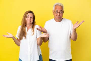 Middle age couple isolated on yellow background having doubts and with confuse face expression