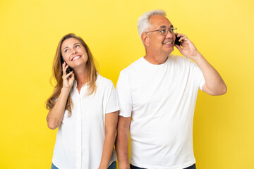 Middle age couple isolated on yellow background talking to mobile