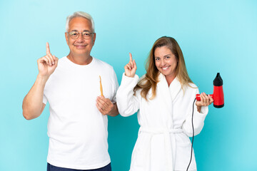 Middle age couple holding dryer and toothbrush isolated on blue background showing and lifting a finger in sign of the best