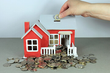 A Hand Adding A Pound Coin To A Model House. Putting Money In To Property Concept.