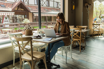 Stylish woman using laptop near dessert and coffee in cafe.