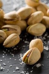 Macro of salted, roasted green pistachio nuts snack on black background with sea salt, healthy food snack