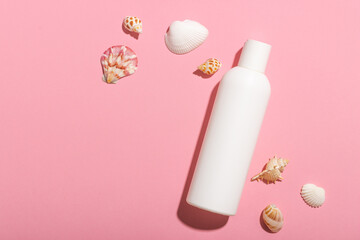 White cosmetic bottle with face cream or lotion and telana against a pink background with seashells. Sun cream, summer cosmetics.