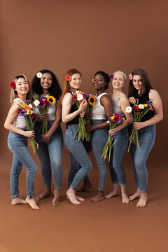 Full body shot of six women of different ages standing together with bouquets of flowers. Smiling women in casuals with flowers in hair.