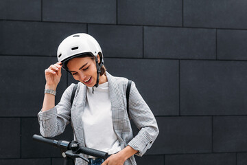 Laughing businesswoman holding a white helmet and looking down at black wall