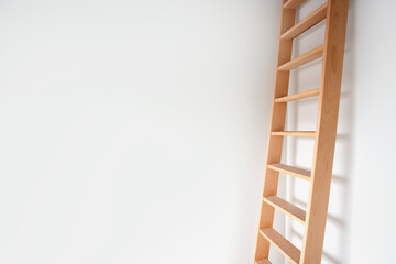 Sideview of a wooden ladder leaning against white wall modern design, stylish stairs in bright room with copy space