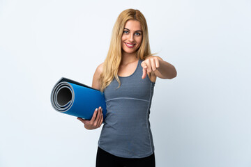 Young sport woman going to yoga classes while holding a mat over isolated white background points finger at you with a confident expression