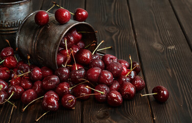 Cherry in water drops in a vintage metal mug are sprinkled on a rustic table. Dark wood background, selective focus. Fresh harvest of juicy cherries