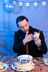 The man is sitting at the table holding a piece of cake and looking at it. Atypical birthday...
