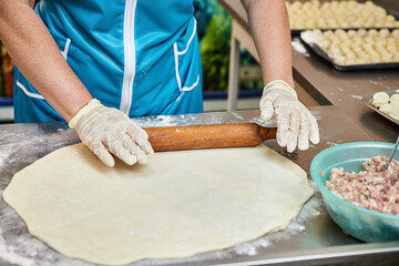 Women chef hands rolls out dough with rolling pin for cooking dumplings, ravioli or khinkali