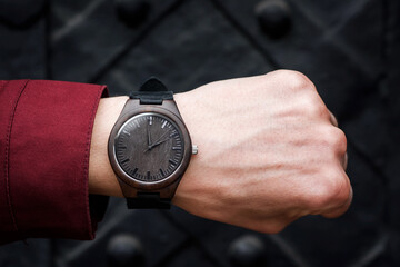 Brown wooden wrist watch with a leather strap on a man's wrist on a black background. Close-up. Space for text. High quality photo