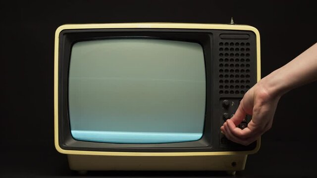Man turning on old retro television on black background, searching for a signal, channel setting. Broken old-fashioned TV with noise screen on table, bad signal reception, cinematography concept.
