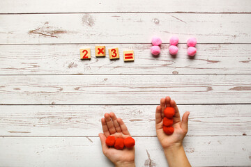 children's hands and counting material, solving examples for multiplication. Top view on a wooden table, light tone. Wooden toys and activities in elementary school