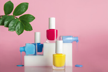 Cosmetic nail polishes on trendy podium. Red, blue and yellow gel polish on pink background with natural leaves. Top view. - obrazy, fototapety, plakaty