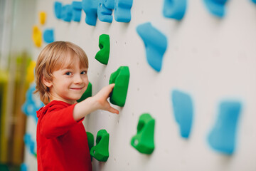 Little boy smile at climbing wall. Children sport, healthy lifestyle in kindergarten or sport center in school.
