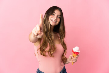 Obraz na płótnie Canvas Young caucasian woman with a cornet ice cream isolated on pink background showing and lifting a finger