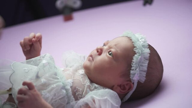 Preparing a newborn girl for a photo session. Little girl in white clothes on a lilac background.