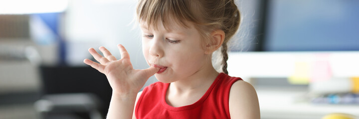 Little girl licking her fingers in front of glass of ice cream