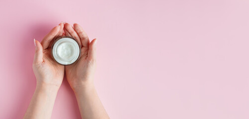 Female hands with a bottle of cream on pink background. Spa and body care concept. Image for advertising.
