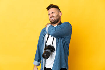 Photographer man isolated on yellow background suffering from pain in shoulder for having made an...