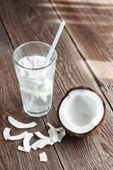 A glass of fresh organic coconut water, milk on a wooden table and a ripe half of a coconut nearby. Refreshing vegetarian drinks