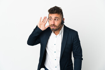 Telemarketer man working with a headset isolated on white background listening to something by putting hand on the ear