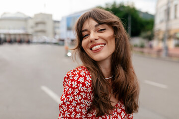 Close up portrait of adorable smiling elegant woman in summer dress posing at camera while walking in the city