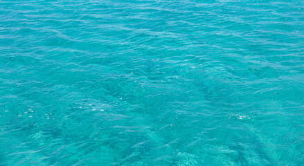 Sea surface blue turquoise color background, some reflections. Calm crystal clear water with small ripples.