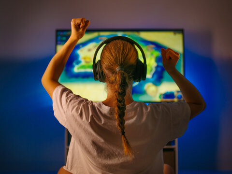 Woman gamer plays video games. In front of her is a computer monitor, headphones are on her head. A woman expresses her emotions violently. Entertainment, spending free time, hobbies.