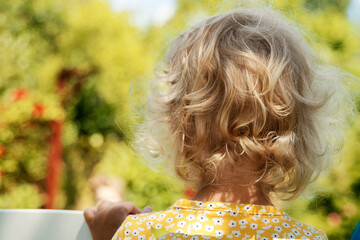 Little girl with blonde curly hair looking away in the garden. 