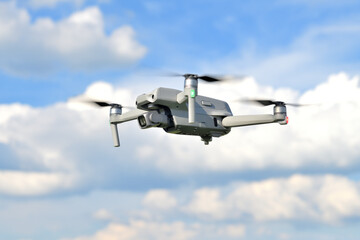 Flying drone quadcopter closeup side view with a blue sky background. UAV drone copter flying with digital camera. View of a photography drone on a blue sky.
