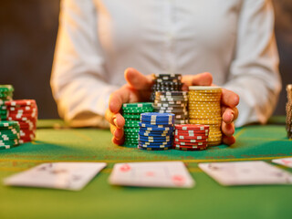 Wealth, luxury, casino gambling. Playing cards are laid out on a table covered with green cloth. The croupier holds a lot of playing chips in his hands. Leisure, hobby, risk.