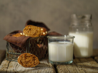 There is a wooden table on which there are walnut cookies, a glass jug and a glass of milk are next...