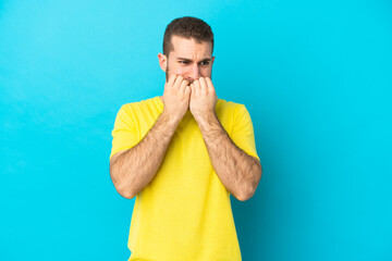 Young handsome caucasian man isolated on blue background nervous and scared putting hands to mouth