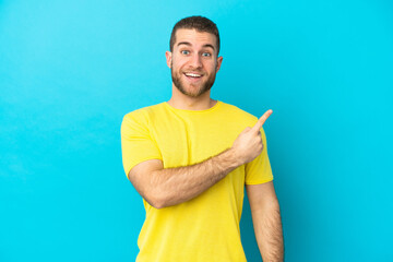 Young handsome caucasian man isolated on blue background surprised and pointing side
