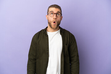 Young handsome caucasian man isolated on purple background looking up and with surprised expression