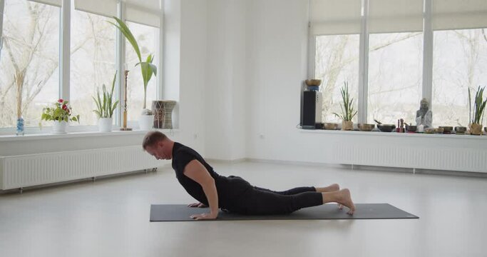 Professional trainer practices flow yoga in private class. Adult man makes yoga asanas on a mat in white bright studio. Fitness, healthy lifestyle and wellness concept.