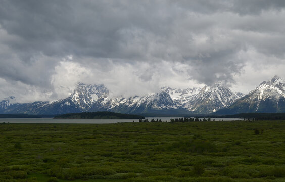 Spring In Grand Teton National Park: Dark Sky Over Willow Flats, Jackson Lake And Donoho Island With Sun Breaking Over Grand Teton, Mount Saint John, Mount Woodring And Mount Moran Of The Teton Range