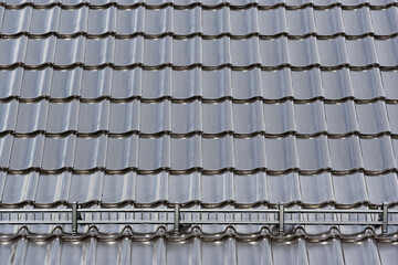 Black porcelain roof shingles tiles in wavy pattern and snow fence with deep shadow contrasts