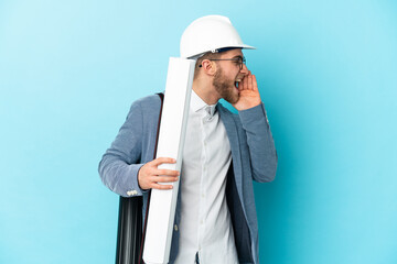 Young architect man with helmet and holding blueprints over isolated background shouting with mouth...