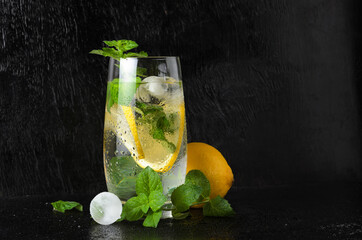 A large glass of water with lemon, mint leaves and ice, covered with water droplets.