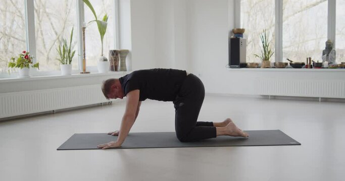 Professional trainer practices flow yoga in private class. Adult man makes yoga asanas on a mat in white bright studio. Fitness, healthy lifestyle and wellness concept.