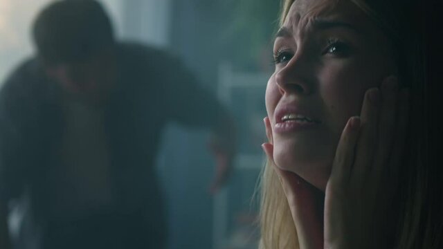 Young wife holding her head and crying close-up. Emotional man shouting at woman in living room, feeling anger and stress, bad mood. Scandals, hysteria and quarrels in family, relationship crisis.