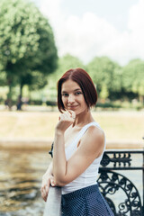 A girl with a bob hairstyle Caucasian walks in a city park on the bridge and looks at the camera