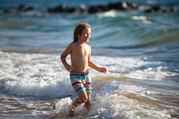 Boy kid jumping in sea waves. Jump by water sea splashes. Summer kids vacation.