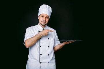 Chef cook wearing cooking jacket and hat, holding a slate plate, on black background