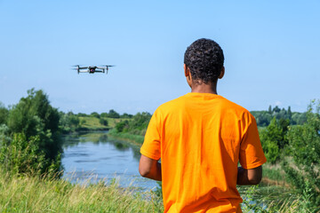 African American man operating drone with controller on the meadow with back