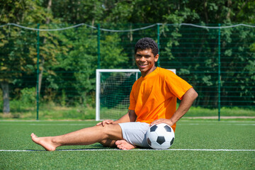 African-American man holding soccer ball while sitting on sports court