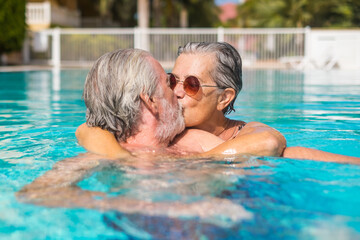 Couple of two happy seniors having fun and enjoying together in the swimming pool smiling and playing. Happy people enjoying summer outdoor in the water. - Powered by Adobe