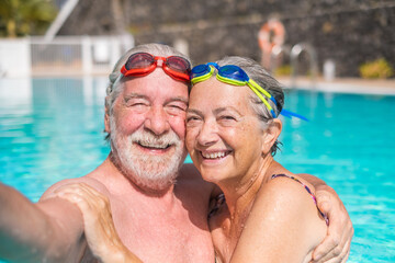 Couple of two happy seniors having fun and enjoying together in the swimming pool taking a selfie...